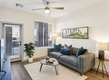 A living room with a grey couch, a painting on the wall, and a ceiling fan.